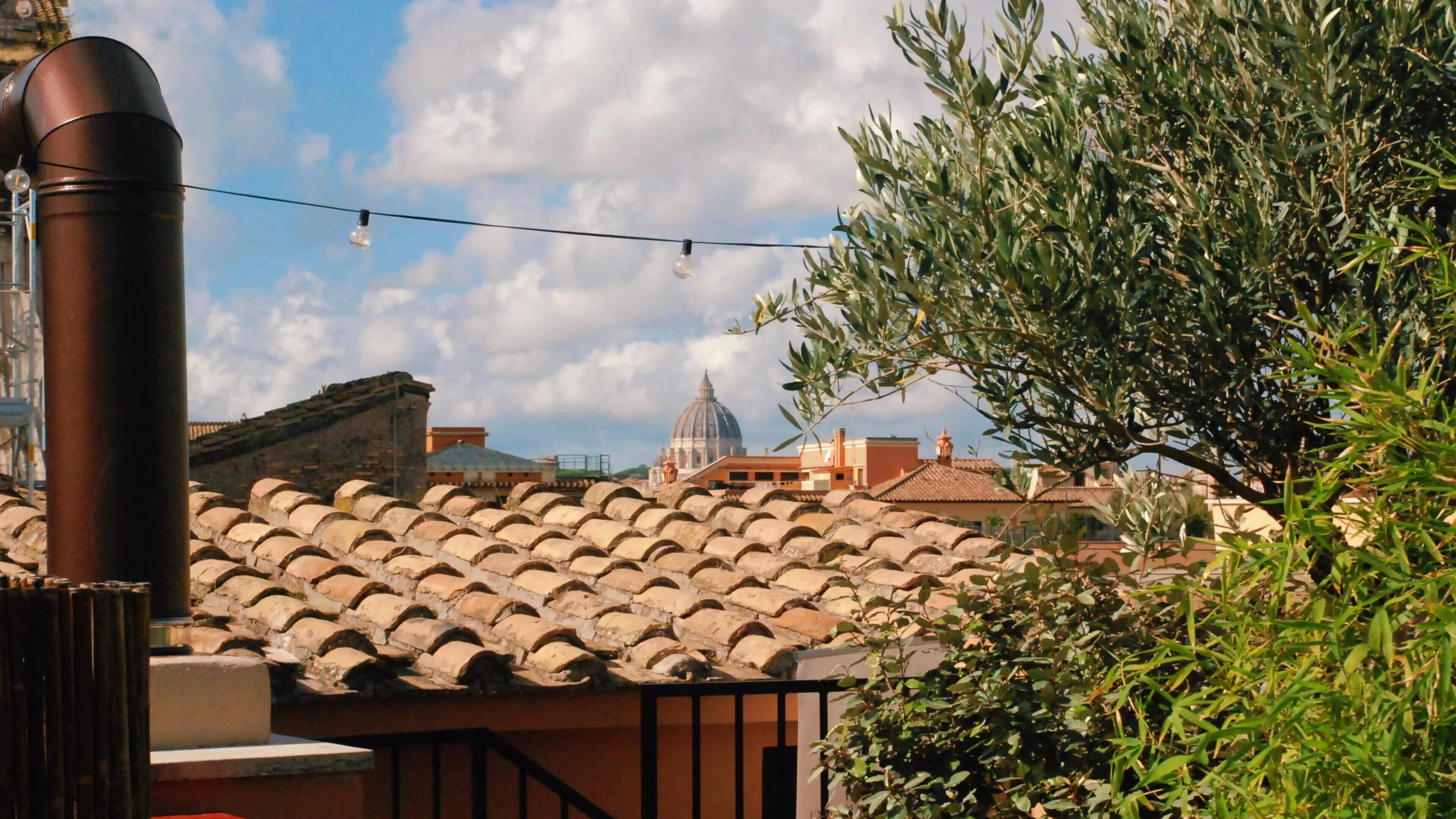 A rooftop terrace with terracotta tiles, a metal chimney, and a view of a historic building with a dome.
