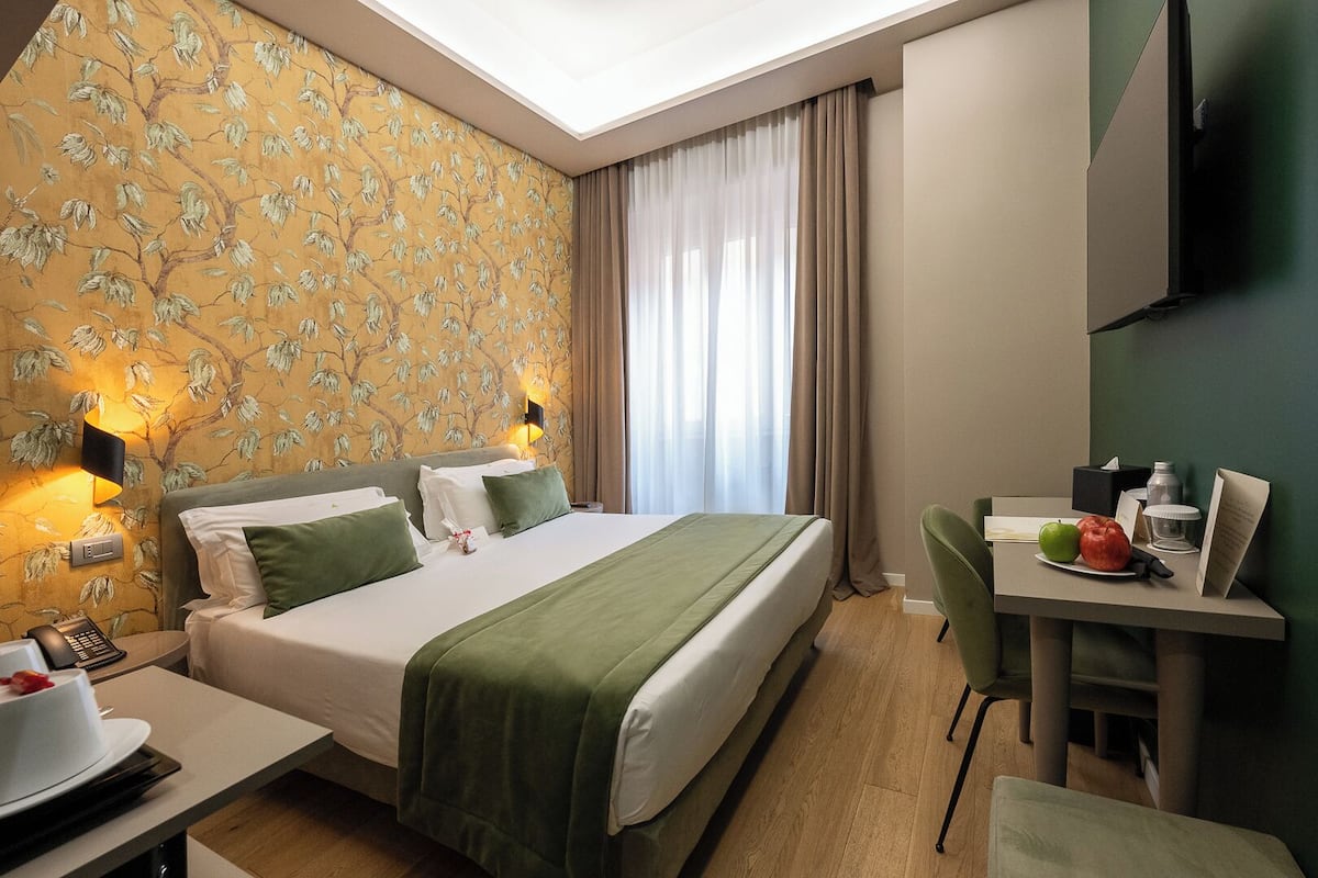 A hotel room with a bed, bedside table, desk, chair, and a TV mounted on the wall.