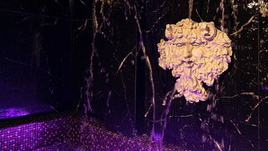 A water feature with a sculptural element, set against a dark background with purple lighting. - Hotel Caravita (Rome)