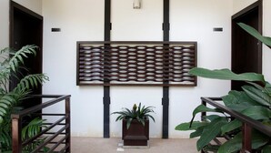 Een gang met een decoratief wandpaneel, een potplant en een trap met een leuning.