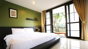 Een slaapkamer met een groot bed, een groene wand, een raam met gordijnen en een klein plankje met een plant.