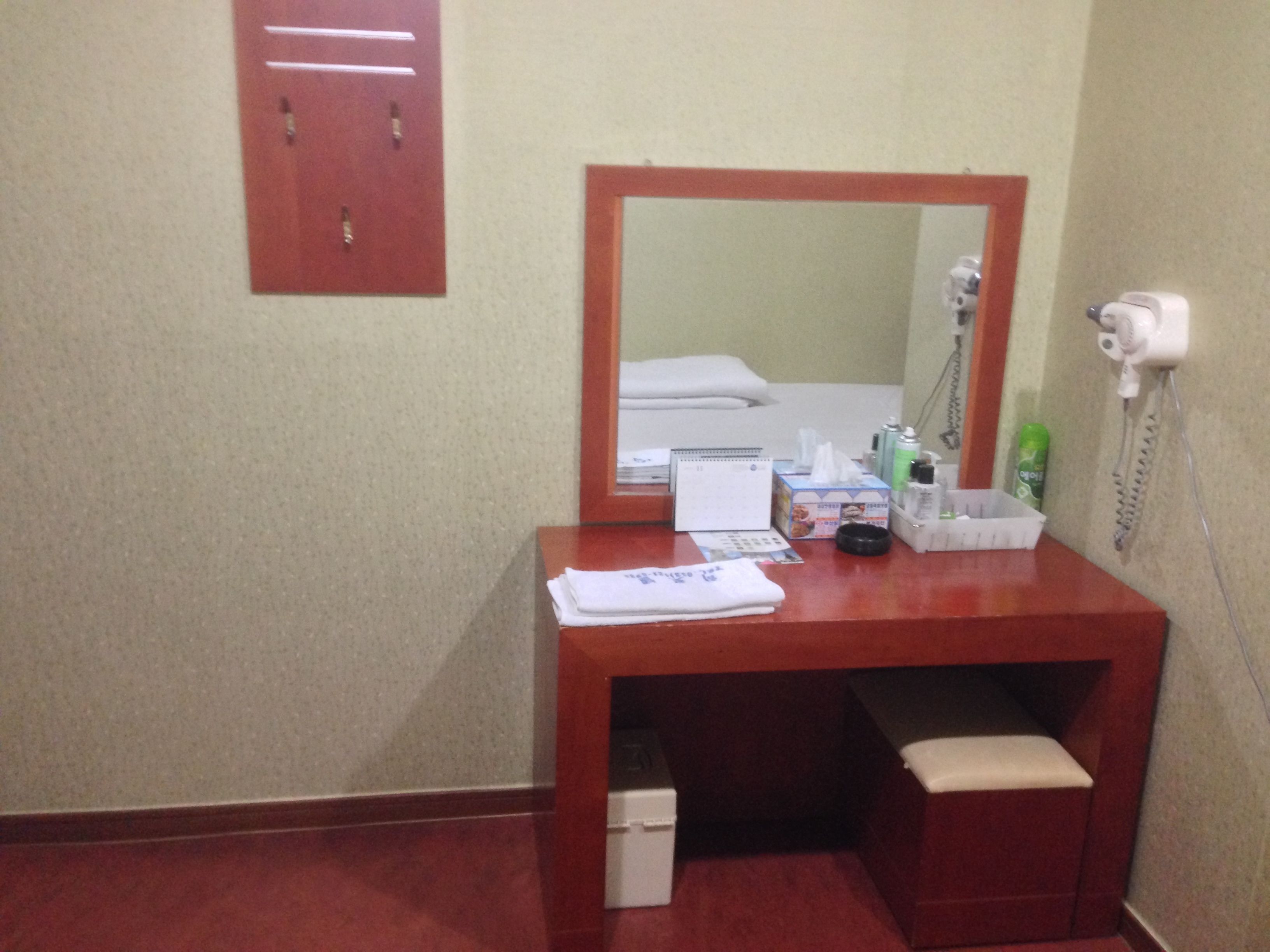 A hotel bathroom with a wooden vanity, a mirror, a sink, a towel, a tissue box, and a hairdryer.