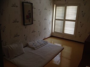 Una habitación con una cama, una ventana con persianas y una pared con motivos florales.