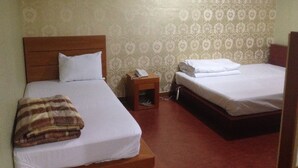 Habitación de hotel con dos camas, cabecero de madera, mesita de noche con teléfono y papel tapiz estampado.