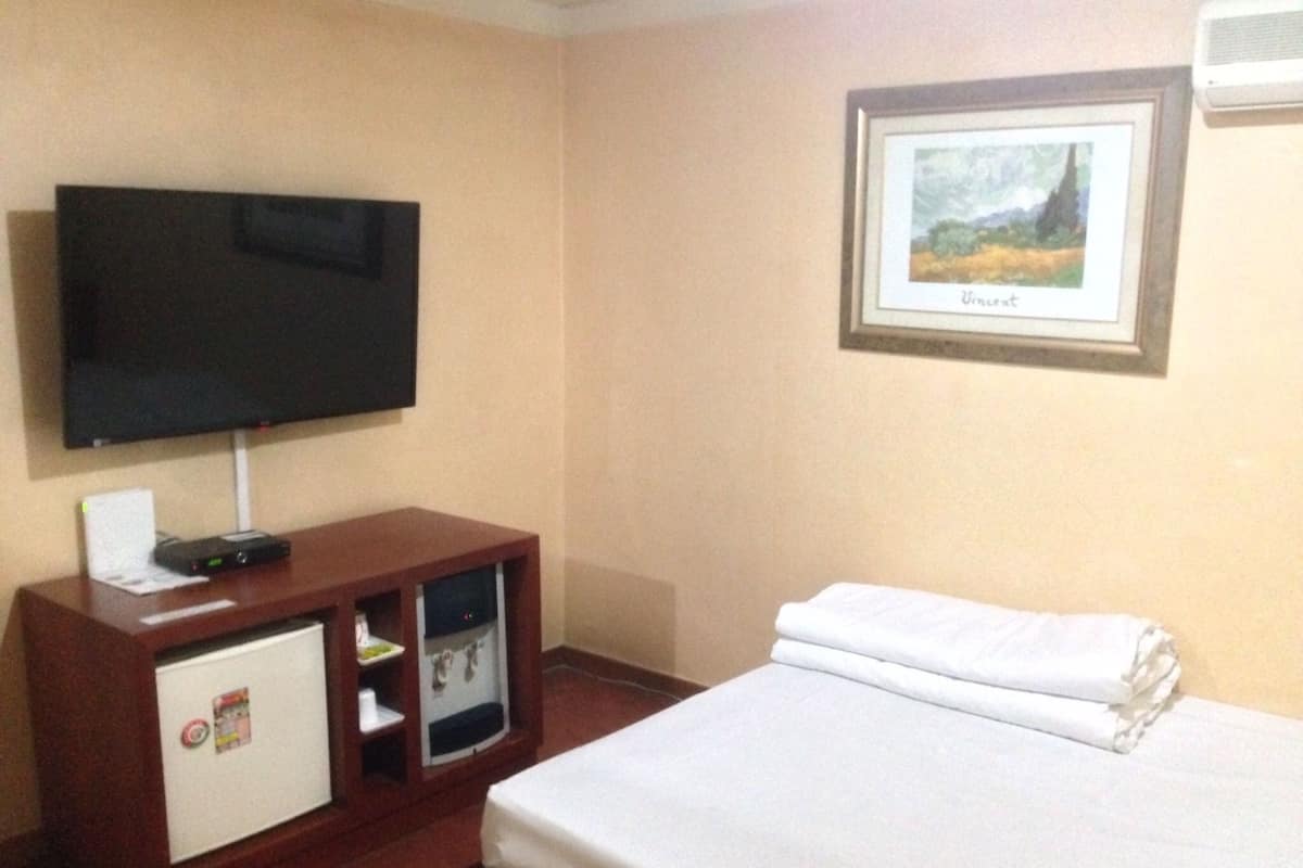 A hotel room with a bed, a TV on a stand, a small cabinet, and a framed picture on the wall.