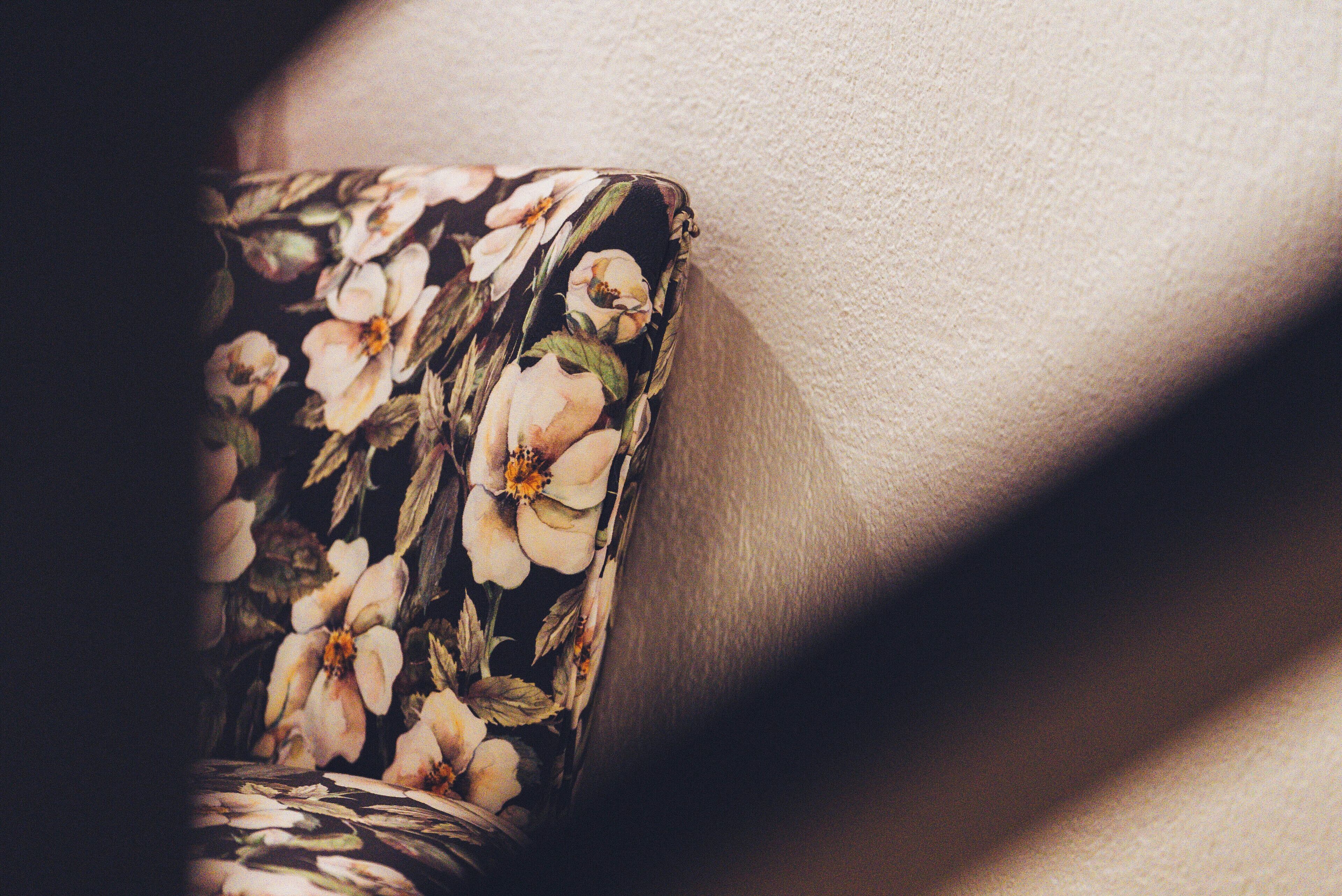 A close-up of a floral-patterned object, possibly a chair or table, against a textured wall.