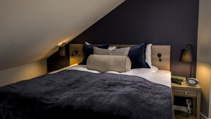 A neatly made bed with a dark blanket, two pillows, and a bedside table with a lamp and books. - Frogner House - Oscars gate (Oslo)