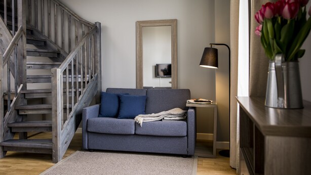A living room with a grey sofa, blue cushions, a wooden staircase, a mirror, a lamp, and a vase with flowers. - Frogner House - Oscars gate (Oslo)