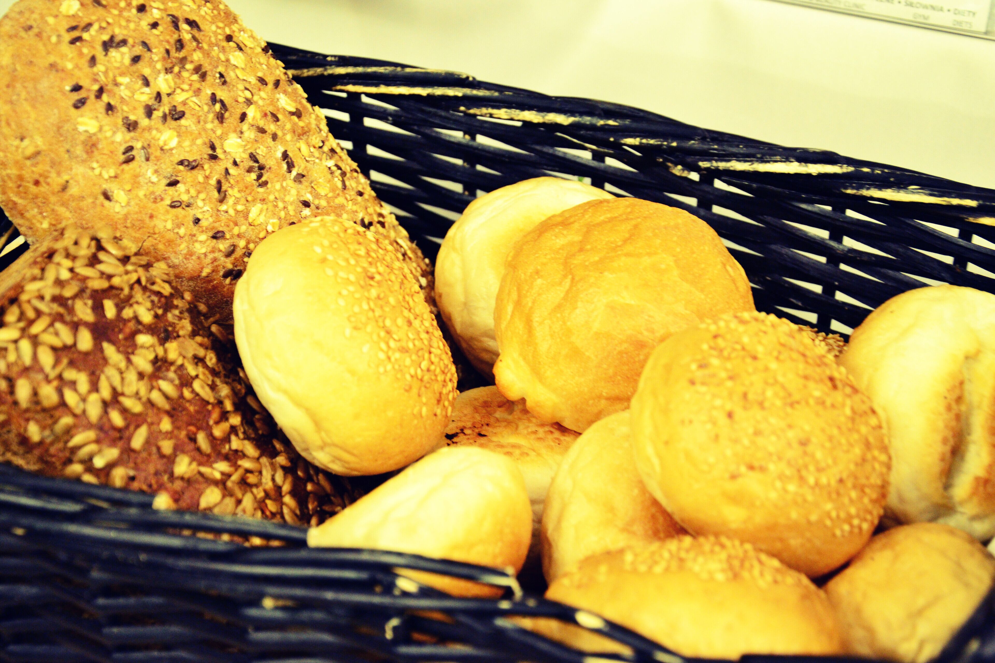 A basket containing various types of bread, including a loaf with seeds and several round buns.