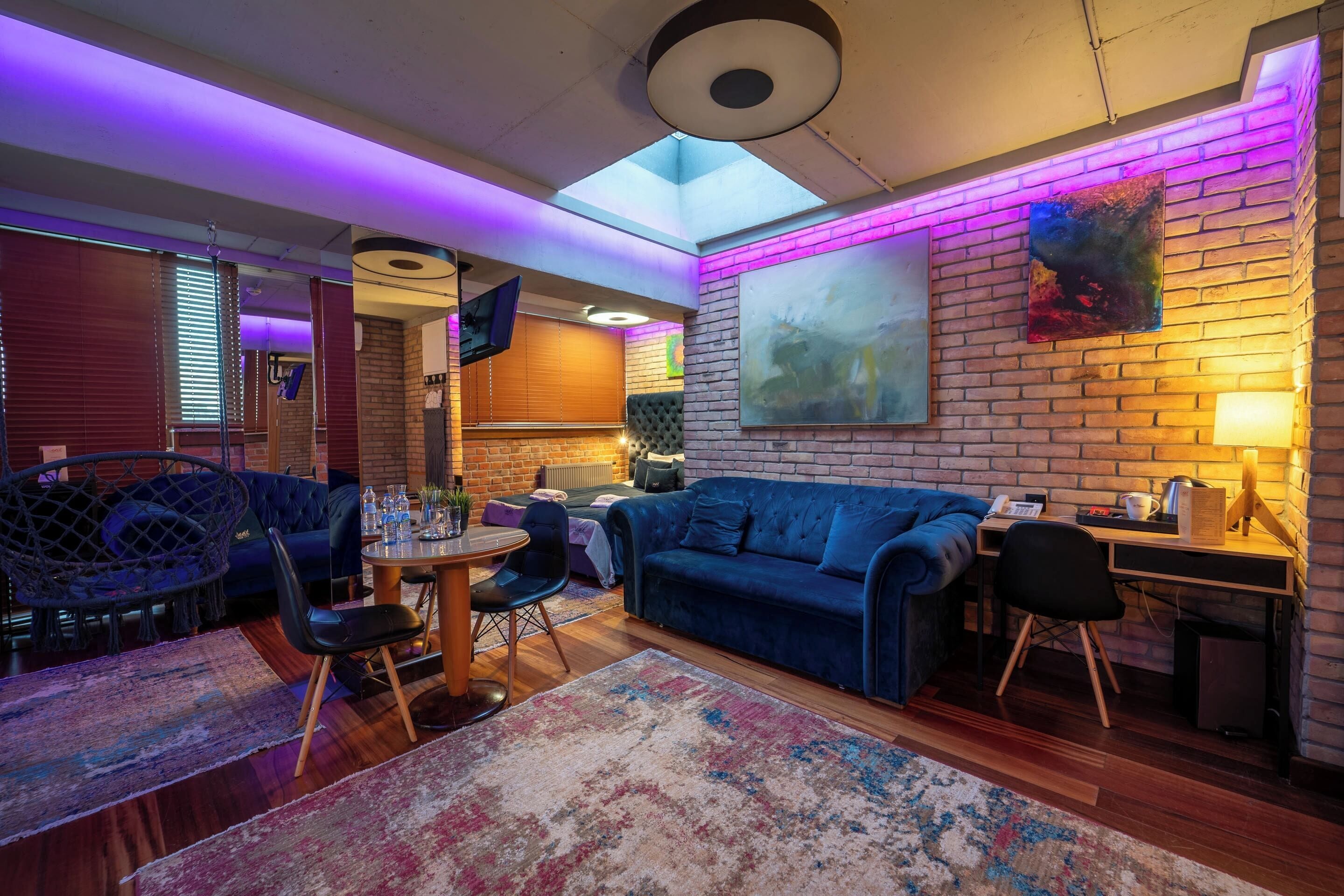 A modern interior with a blue sofa, a dining table, and a brick wall with a painting.