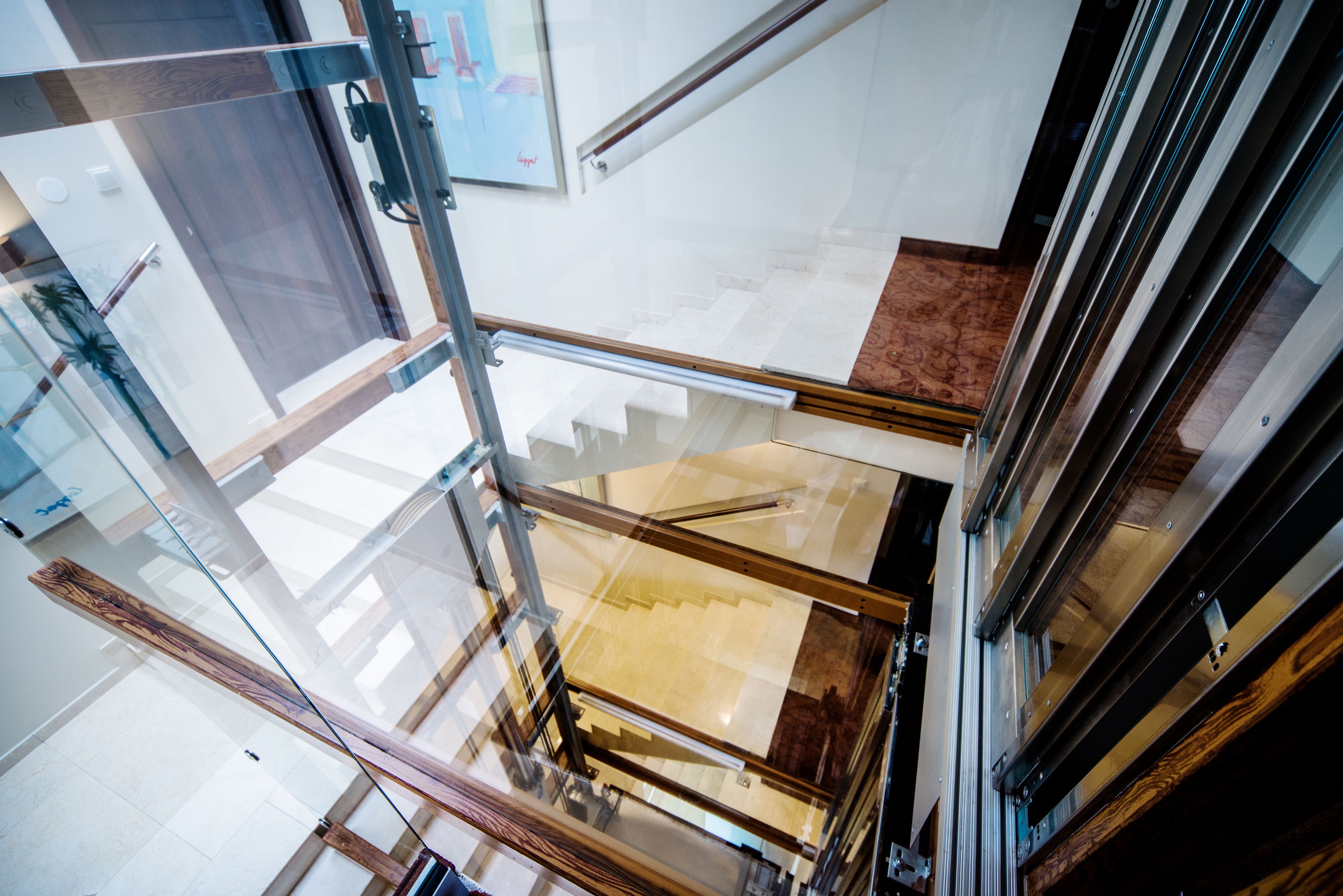A modern interior with glass railings, a wooden floor, and a staircase leading to an upper level.
