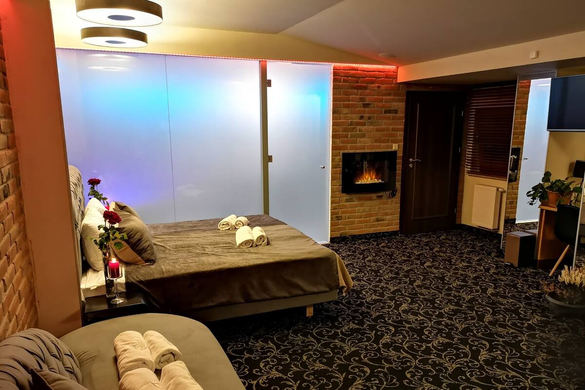 A hotel room with a bed, a sofa, a fireplace, and a brick wall.