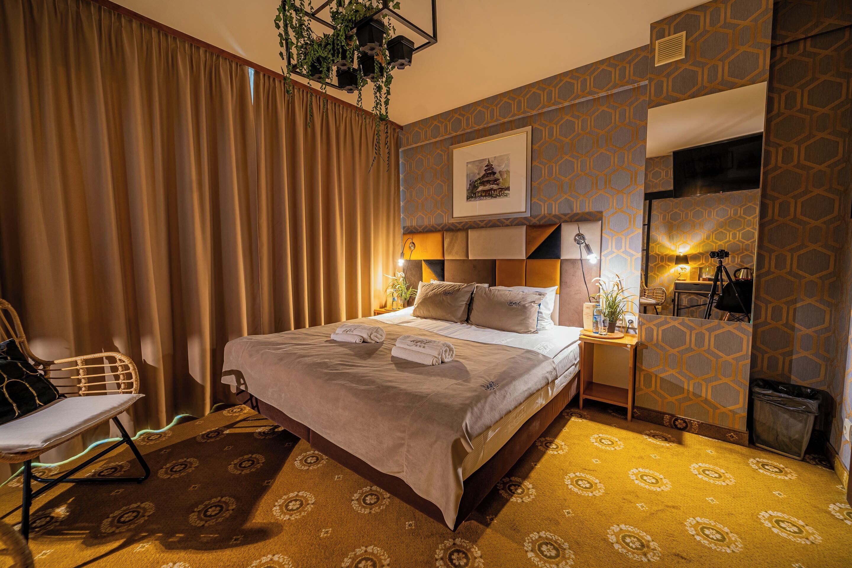 Una habitación de hotel ordenada con una cama grande, una silla, un escritorio con lámpara y un cubo de basura.