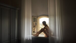 Una habitación con un ventanal grande, un armario y una persona sentada junto a la ventana.