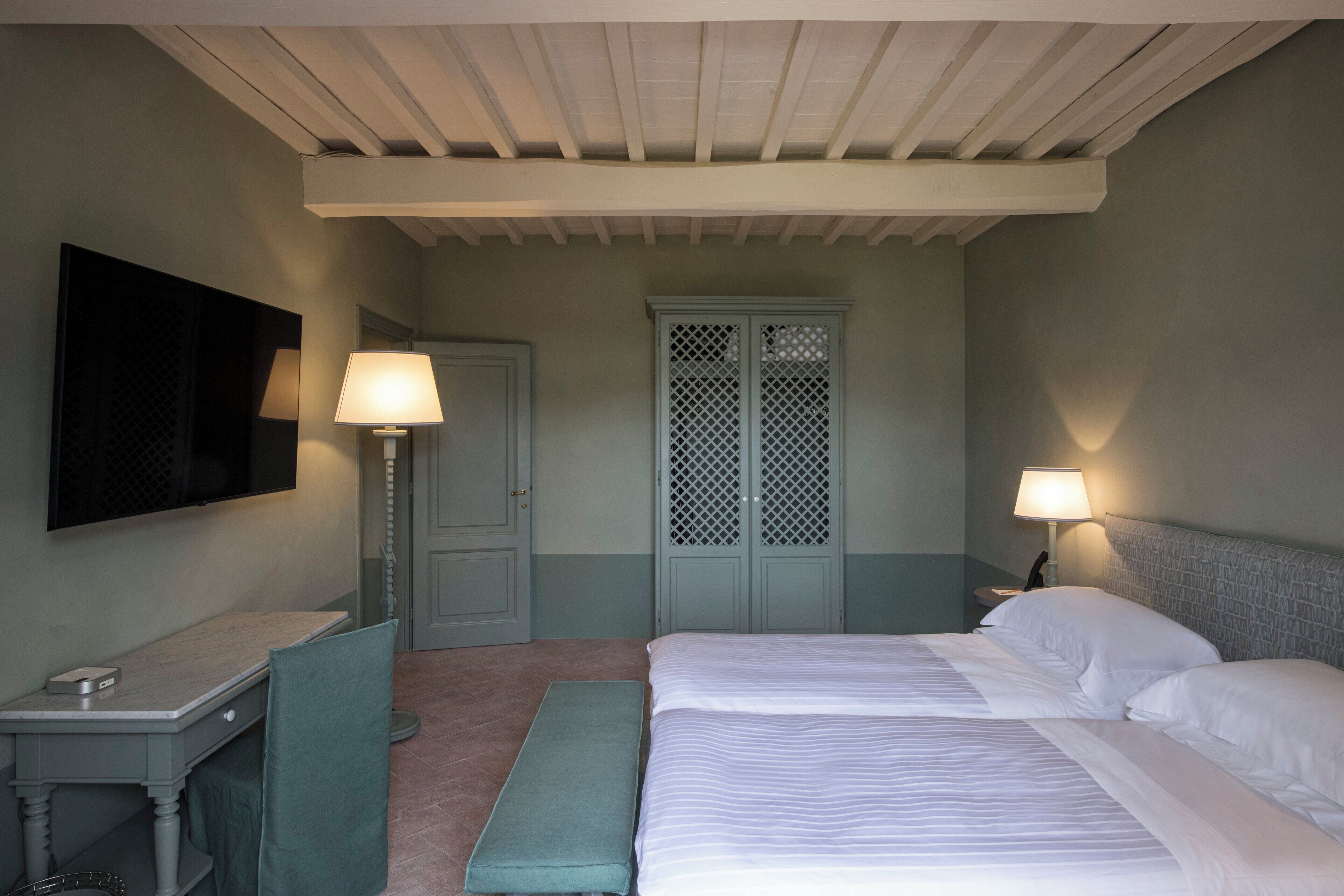 Hotelkamer met een bed, bureau, stoel, bank, televisie en raam met een lattenwerk ontwerp.