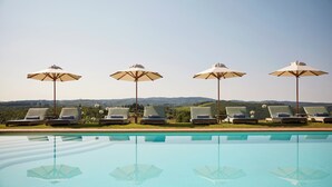 Zona junto a la piscina con sillones de descanso y sombrillas, cielo despejado y vistas al paisaje.