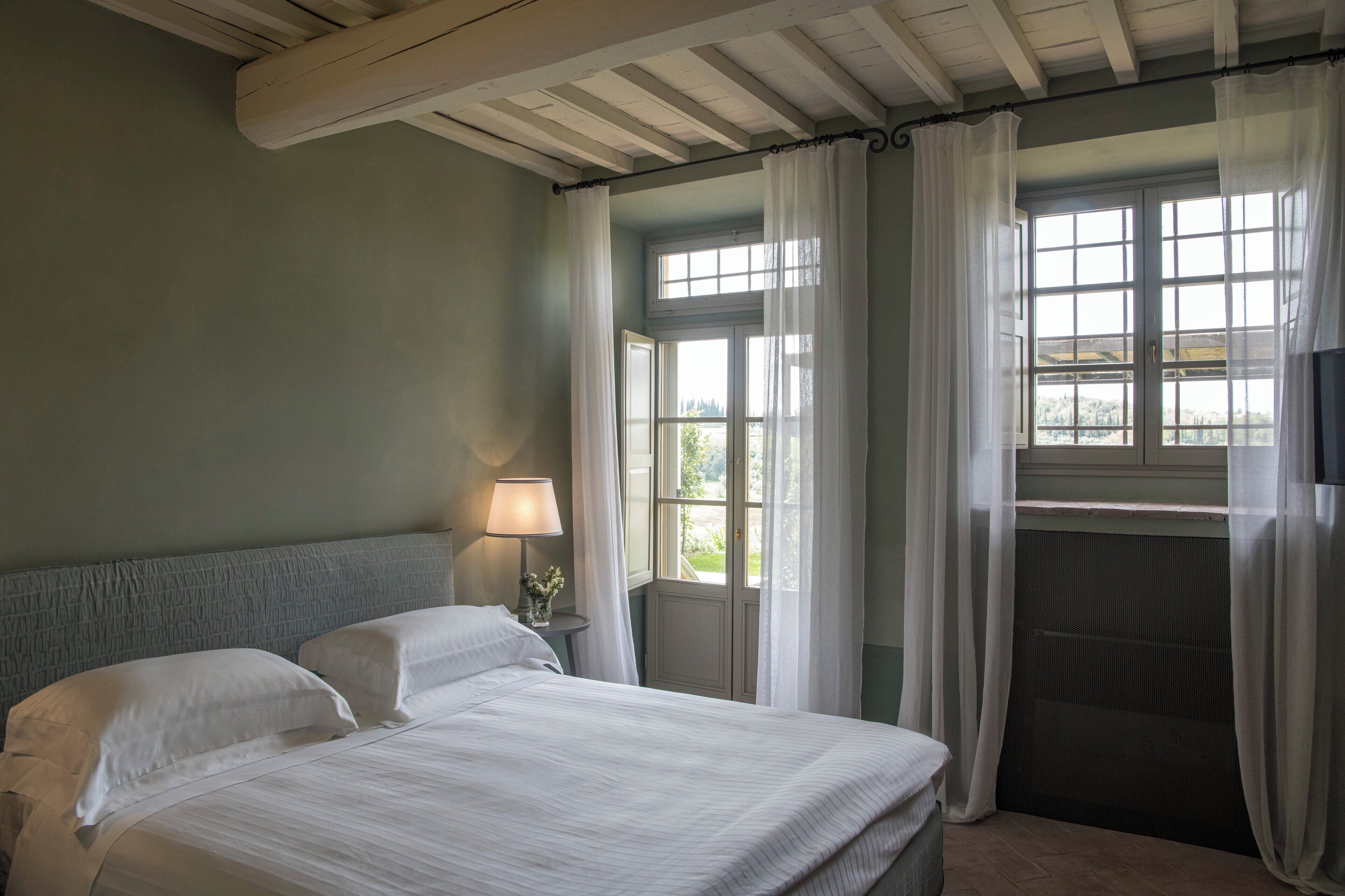 A bedroom with a bed, a nightstand, a lamp, and a window with curtains.