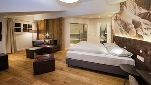 A modern bedroom with a large bed, a sofa, a desk, and a wooden accent wall. - HEITZMANN - Hotel & Rooftop (Zell am See)