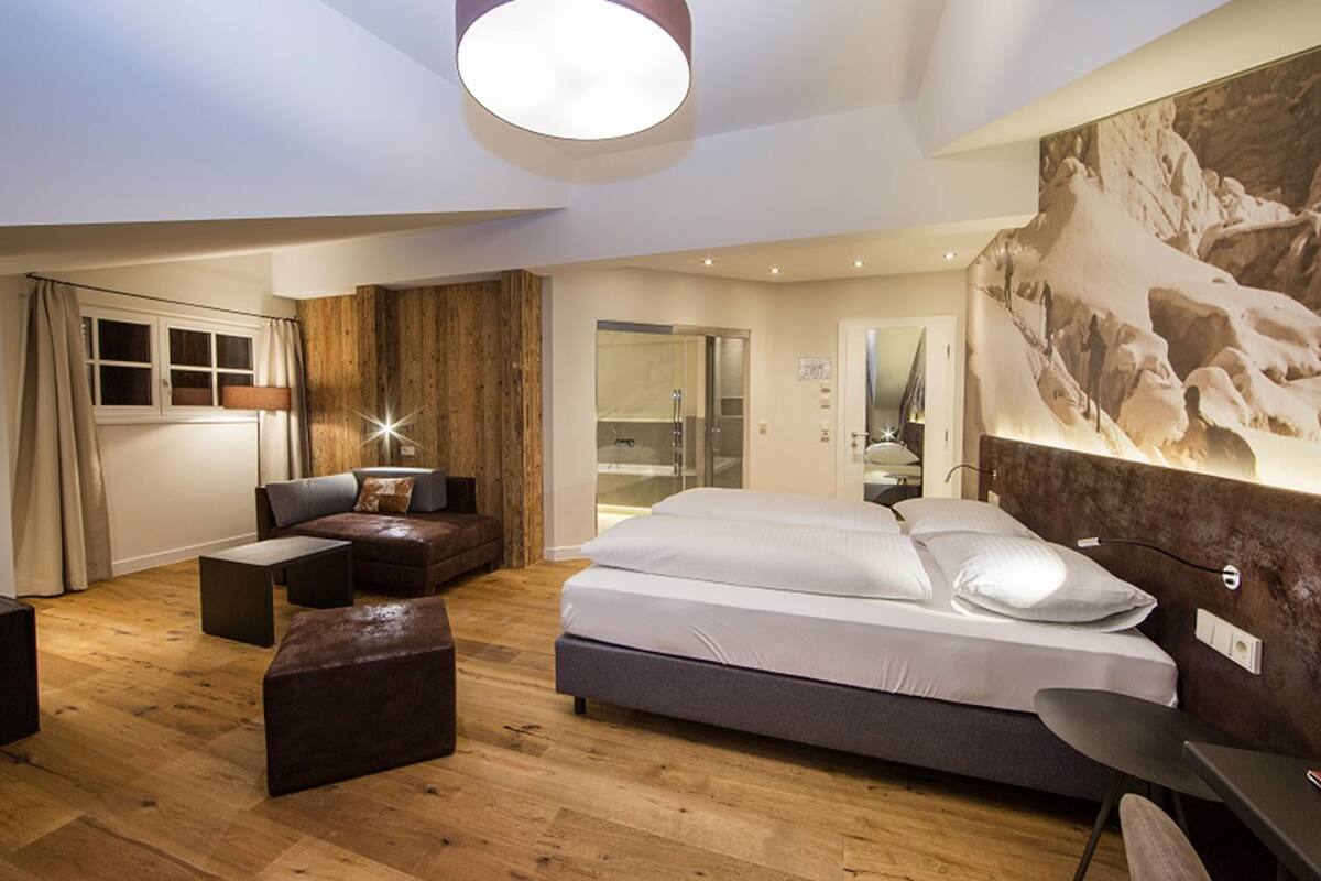 A modern bedroom with a large bed, a sofa, a desk, and a wooden accent wall.