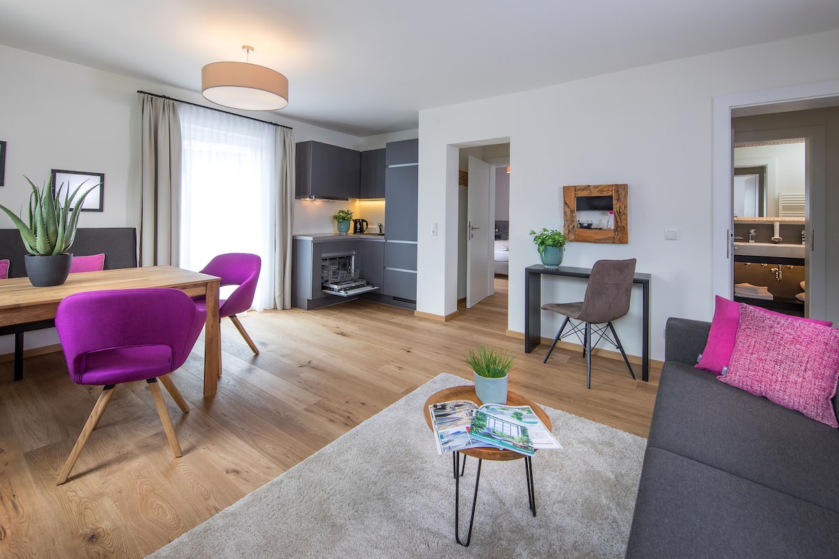 A modern living room with a dining area, a kitchen, and a bathroom.
