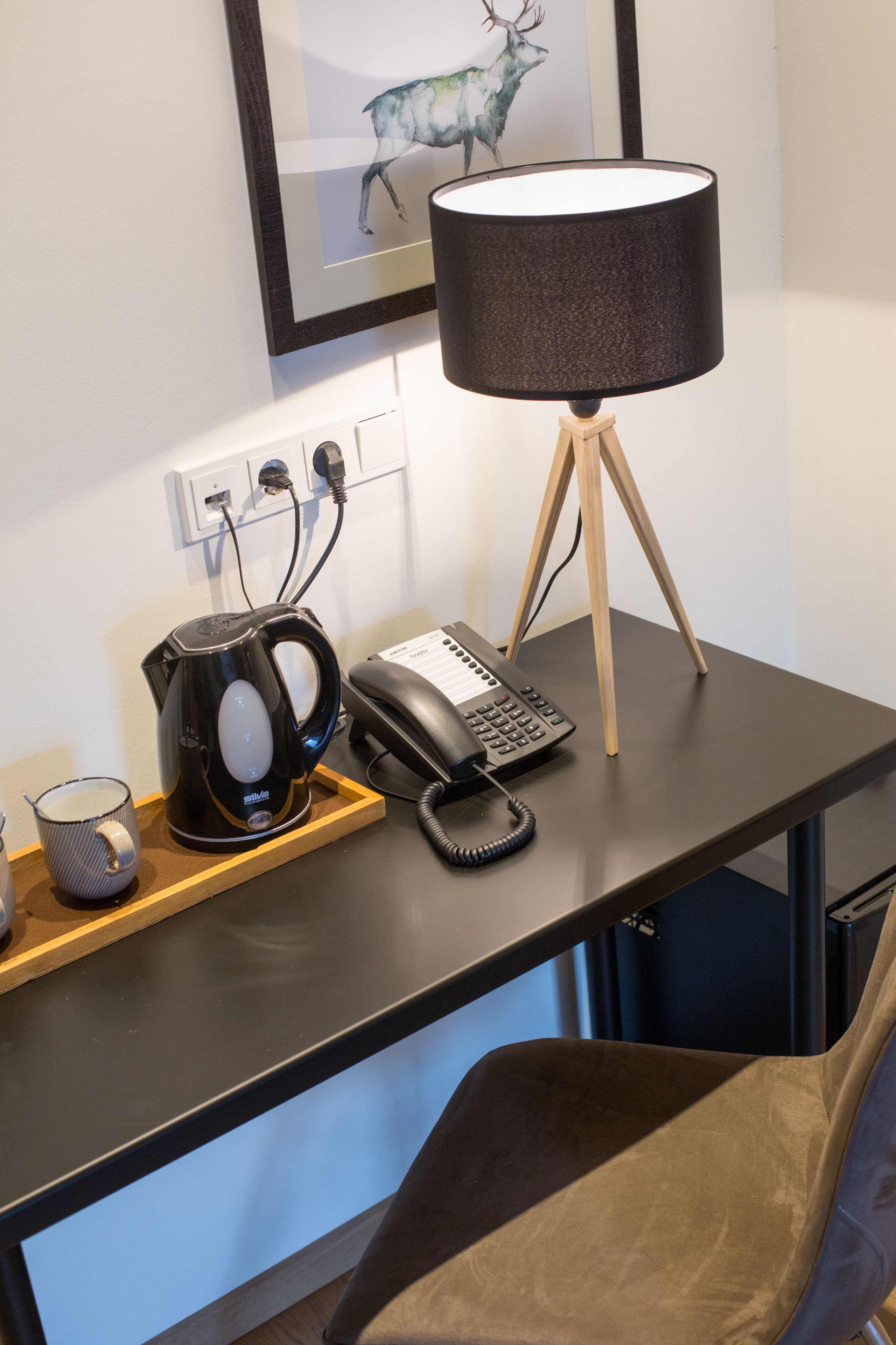 Ein Schreibtisch mit einer Lampe, einem Telefon, einem Wasserkocher und einer Tasse.