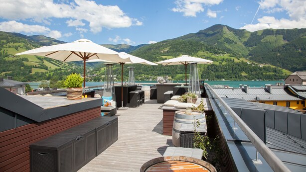 A rooftop terrace with outdoor seating, umbrellas, and a scenic mountain view. - HEITZMANN - Hotel & Rooftop (Zell am See)