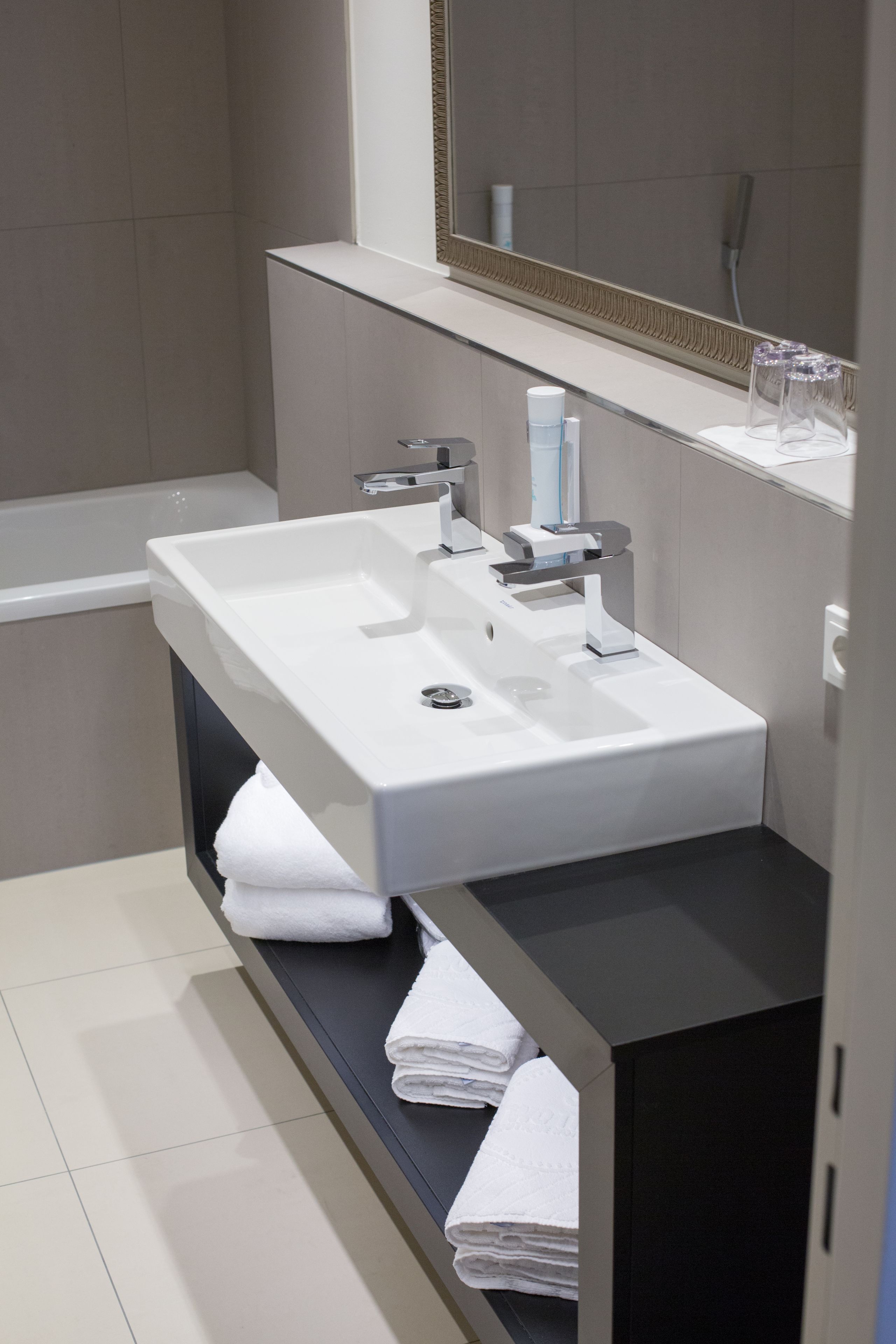 A modern bathroom with a white sink, a mirror, and a towel rack.
