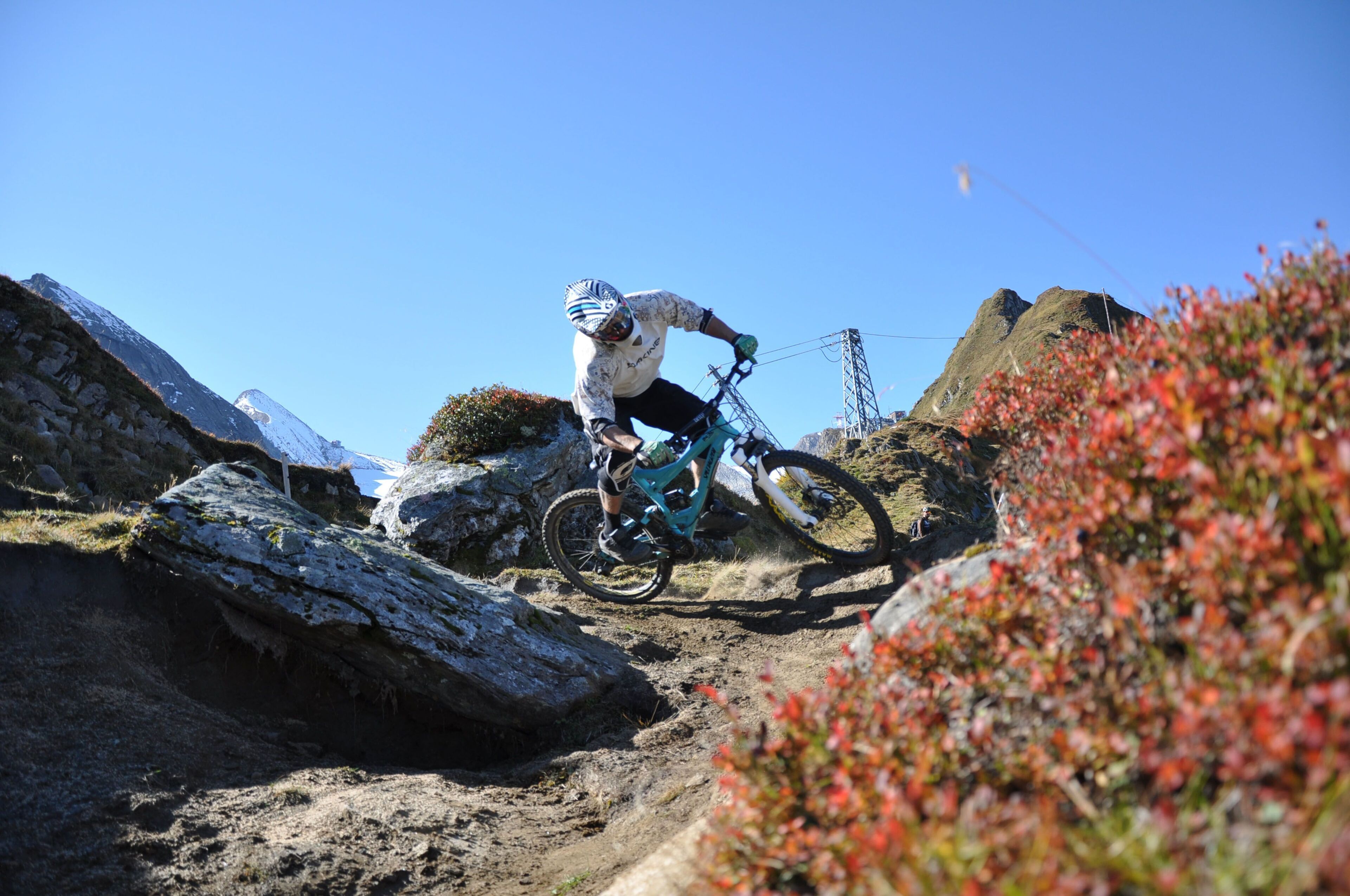 Ein Mountainbiker bewegt sich auf einem steinigen Weg, im Hintergrund ein klarer, blauer Himmel.
