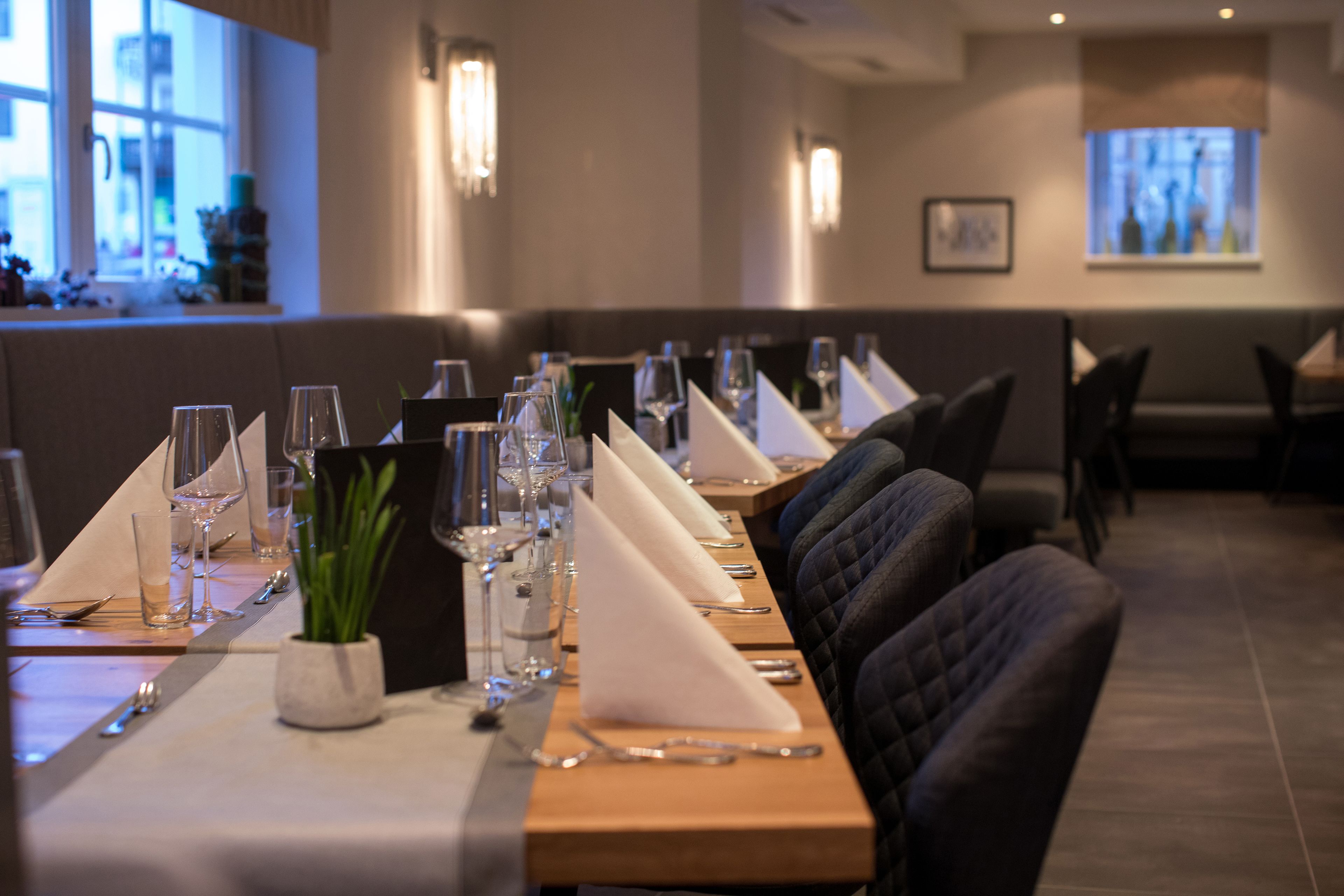 A restaurant with a long table set for a meal, including wine glasses, cutlery, and napkins.