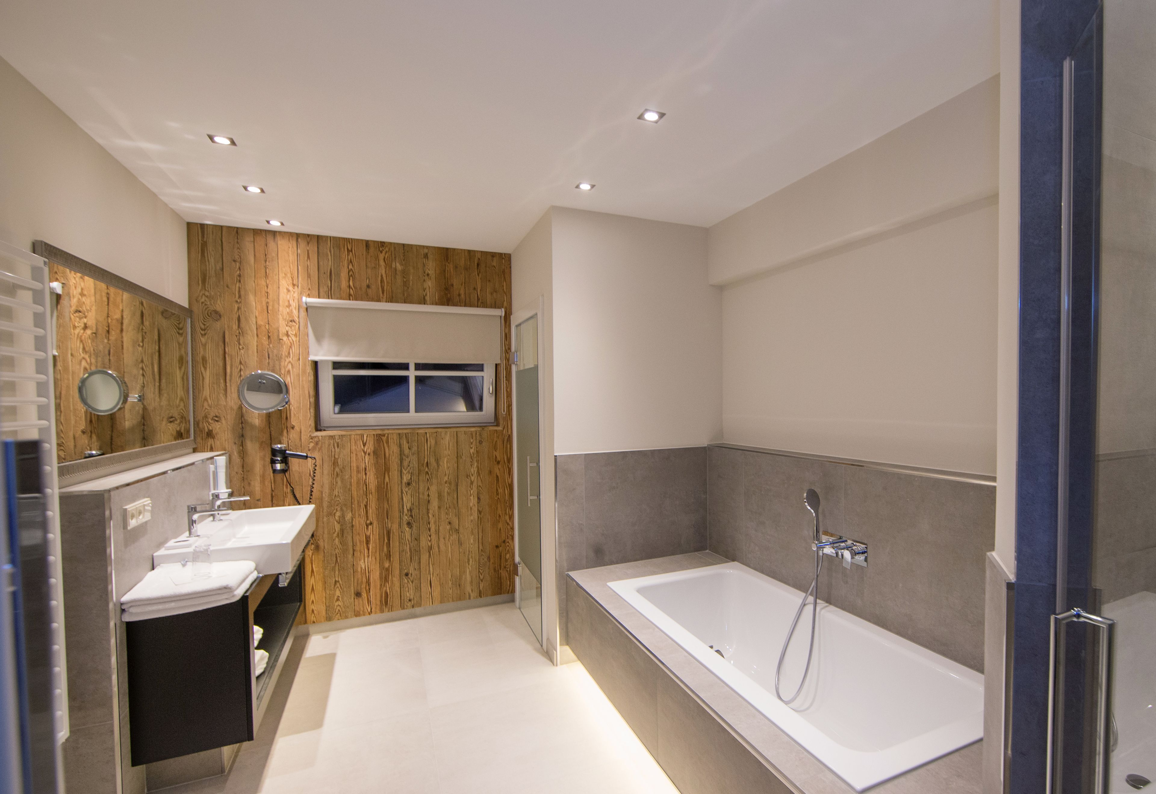 A modern bathroom with a wooden accent wall, a large bathtub, and a vanity with a mirror.