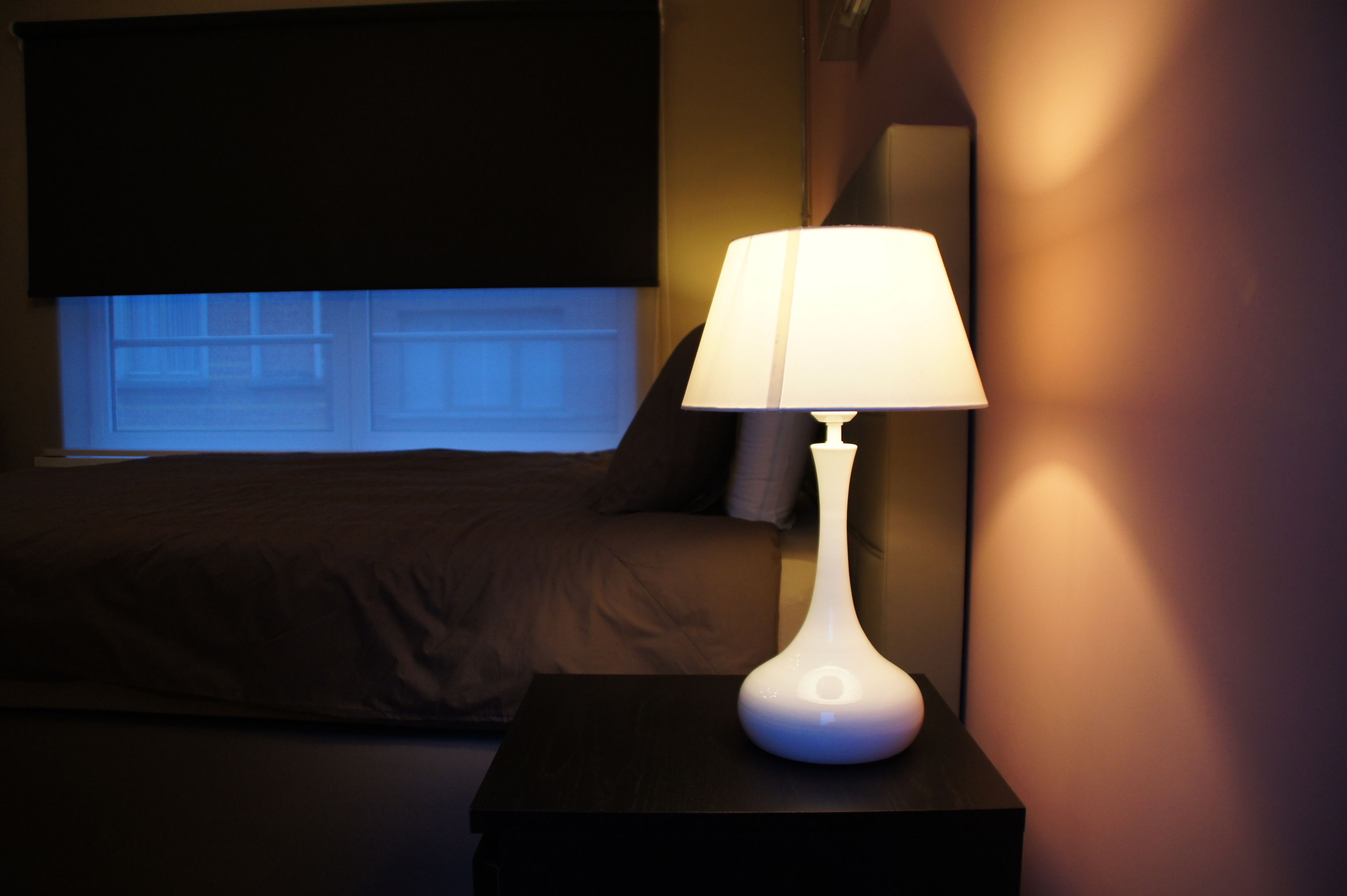 A bedroom with a bed, a nightstand with a lamp, and a window with blinds.