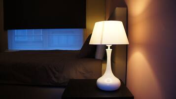 A bedroom with a bed, a nightstand with a lamp, and a window with blinds.