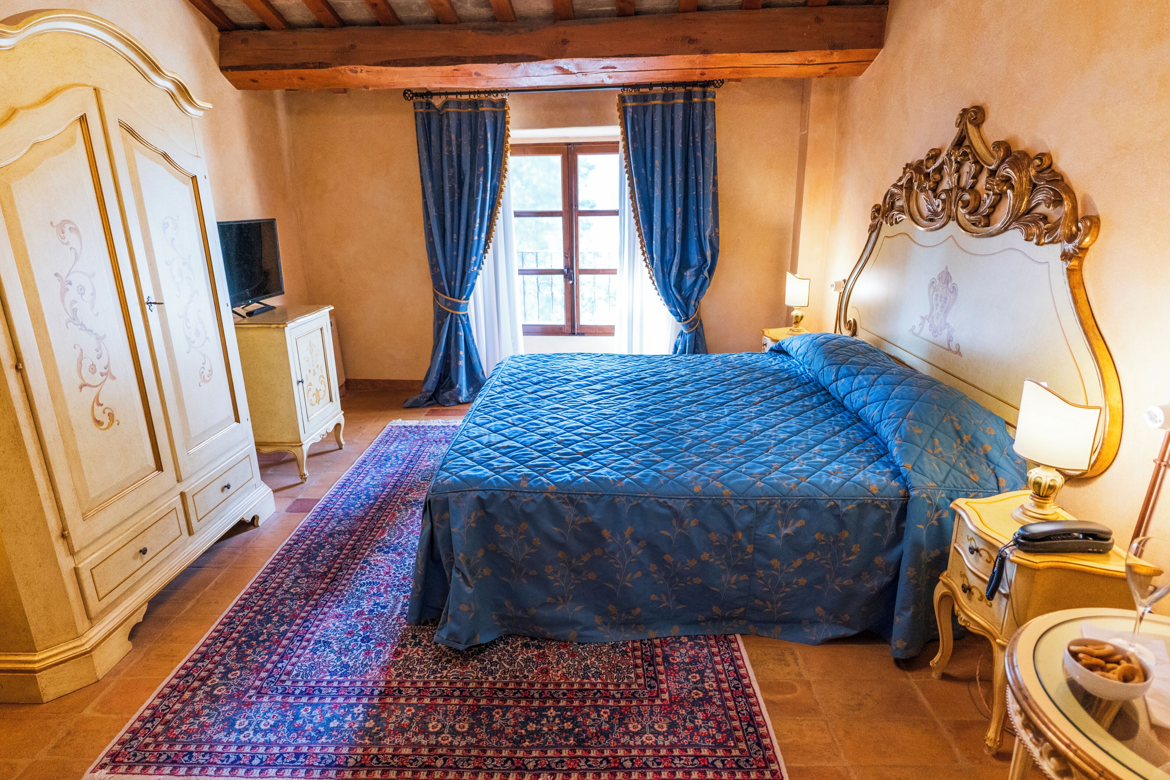 A bedroom with a large bed, a dresser, a nightstand with a lamp, and a window with curtains.