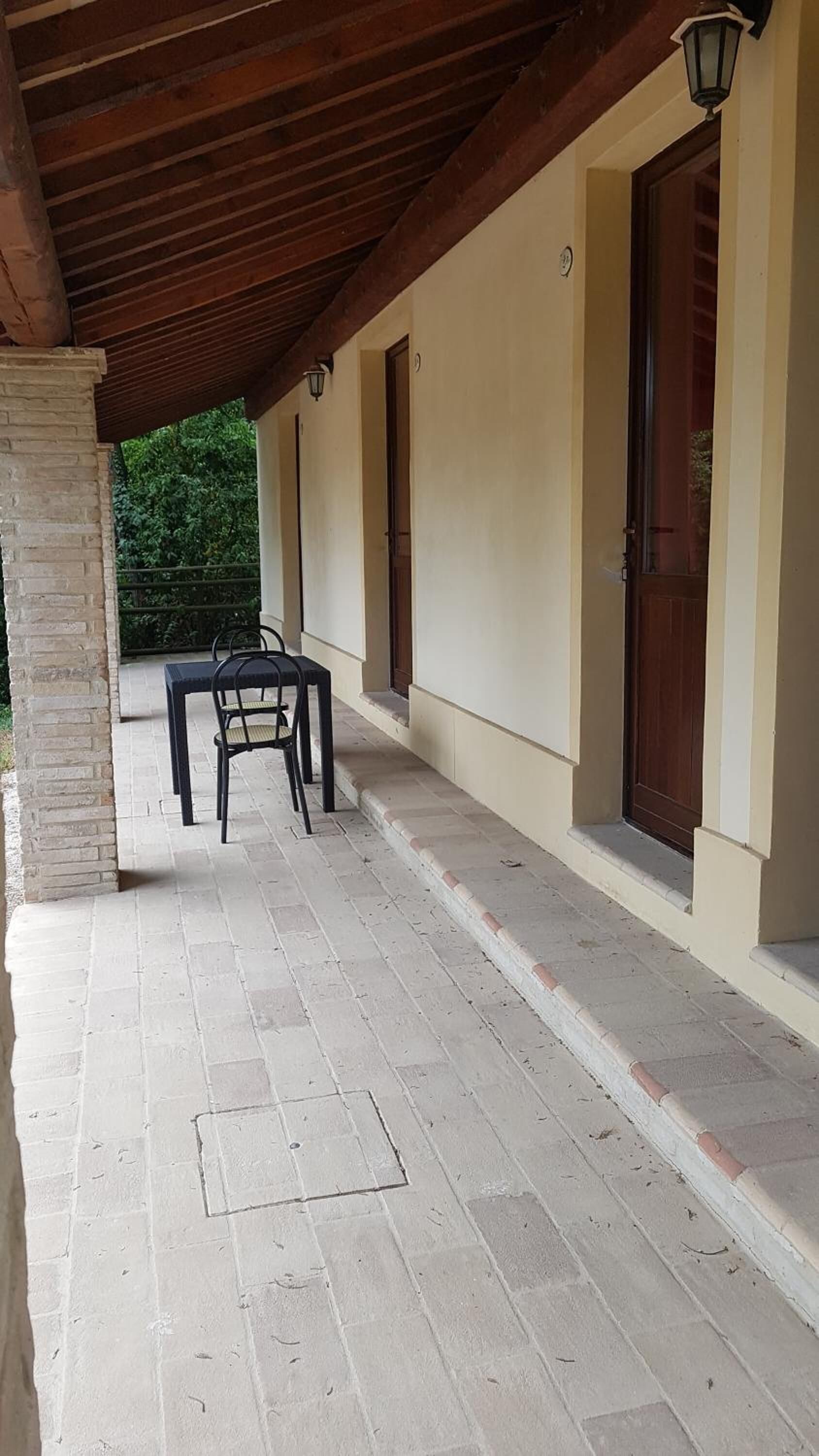 A covered outdoor area with a table and chairs, a wooden ceiling, and a beige wall with a door.