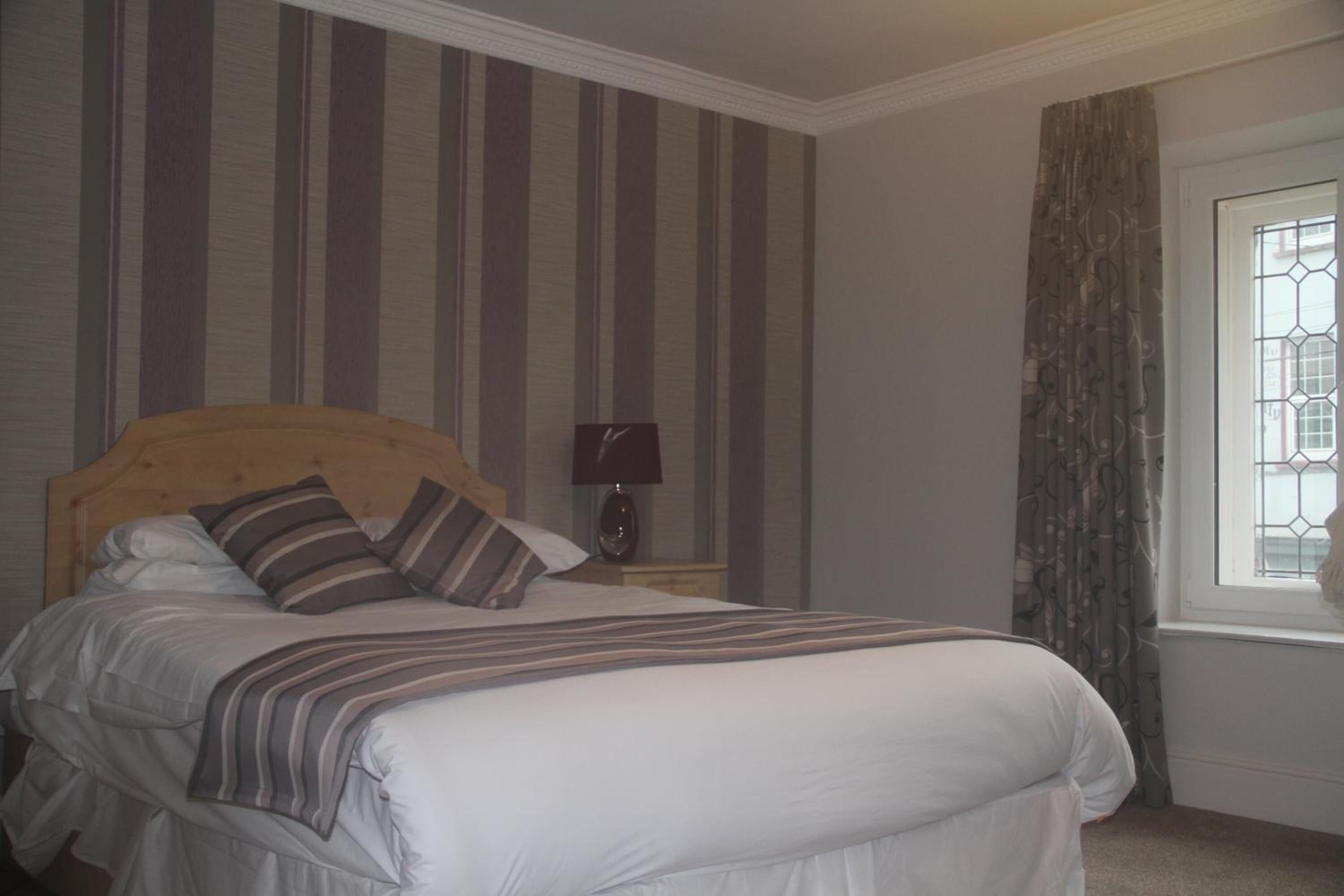 A neatly made bed with striped bedding, a wooden headboard, and a bedside lamp.