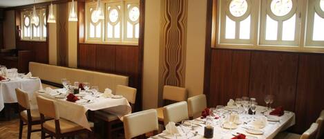 A restaurant with long tables set for dining, wooden paneled walls, and large windows with decorative glass panels.