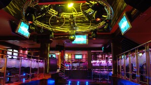 Un bar con estructura de techo circular, múltiples pantallas y una barra con taburetes.
