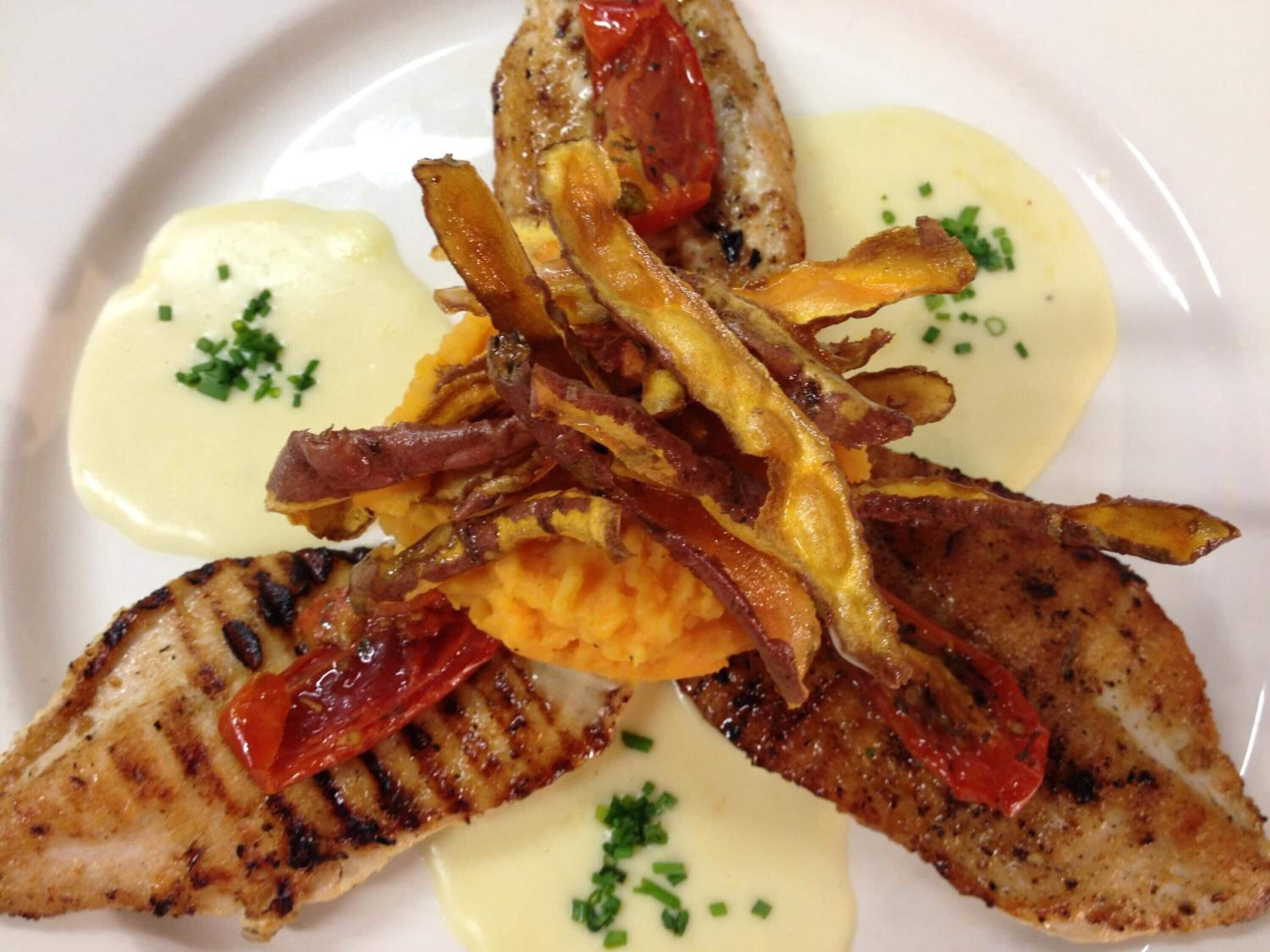 A plate of food with grilled fish, roasted potatoes, and a creamy sauce.