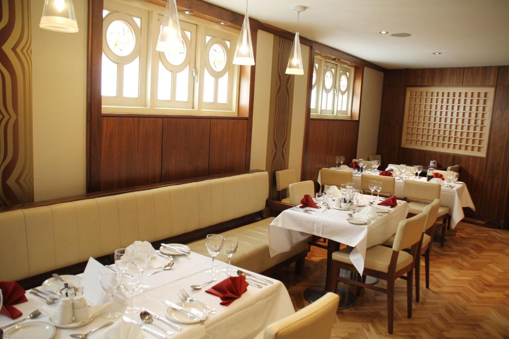 A restaurant with multiple tables set for dining, wooden paneling on the walls, and pendant lighting.