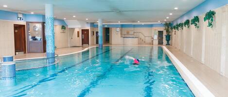 An indoor swimming pool with clear lanes, a lifeguard chair, and a reception desk.
