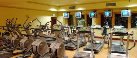 A gym with multiple treadmills and elliptical machines, equipped with digital screens and weight benches.