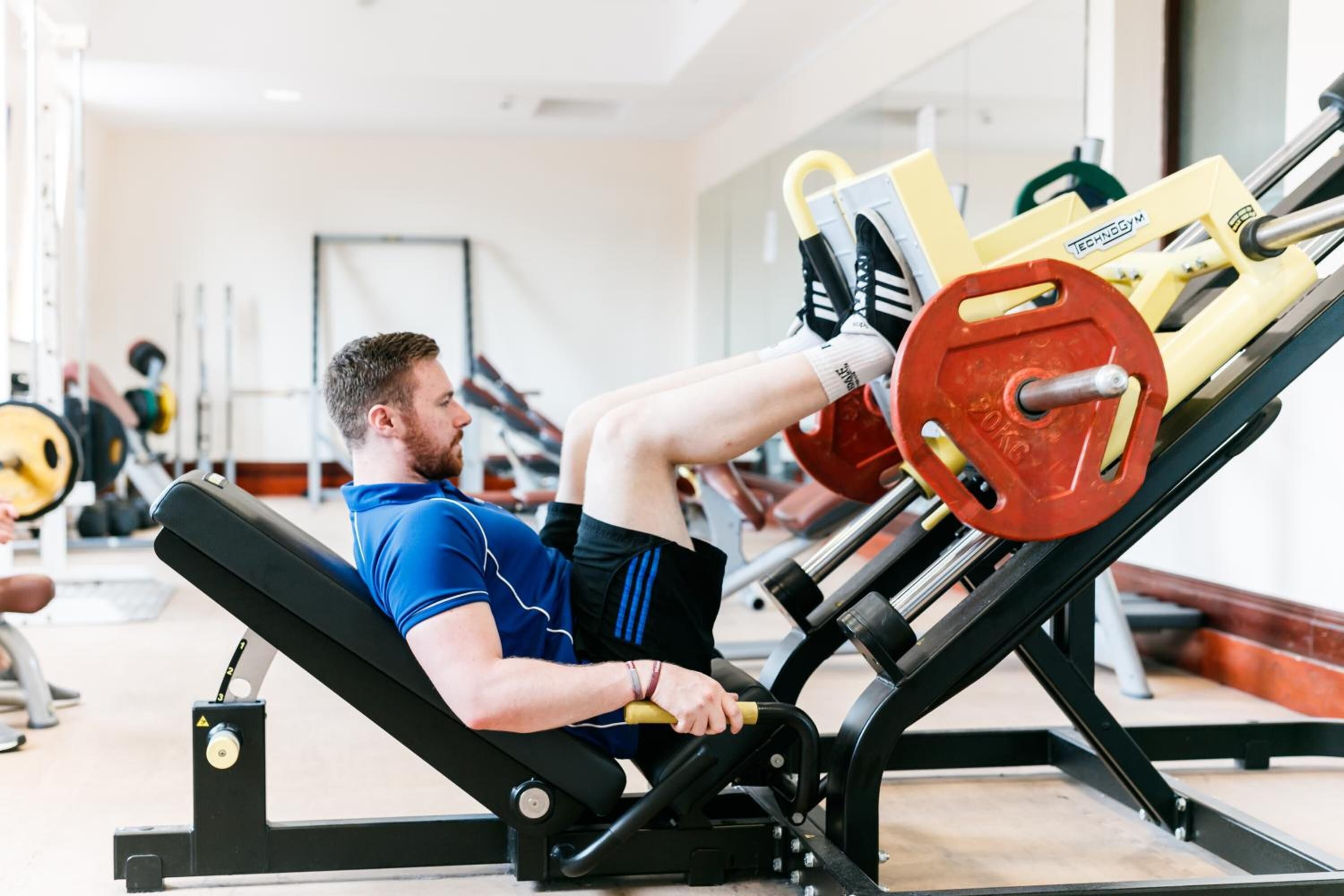 A gym with a person using a leg press machine.