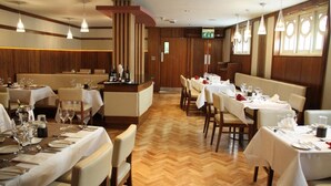 Un restaurante con varias mesas dispuestas para comer, paneles de madera en las paredes e iluminación colgante.