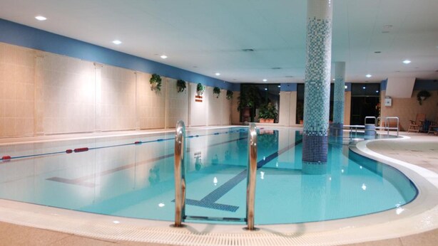 Una piscina interior con carriles delimitados, suelo de azulejos y un pilar revestido de cerámica.