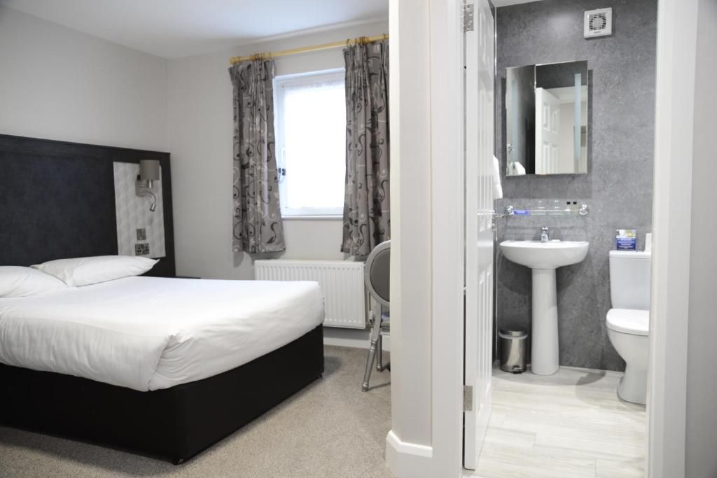 Un dormitorio con cama, ventana con cortinas, radiador y baño con lavamanos e inodoro.