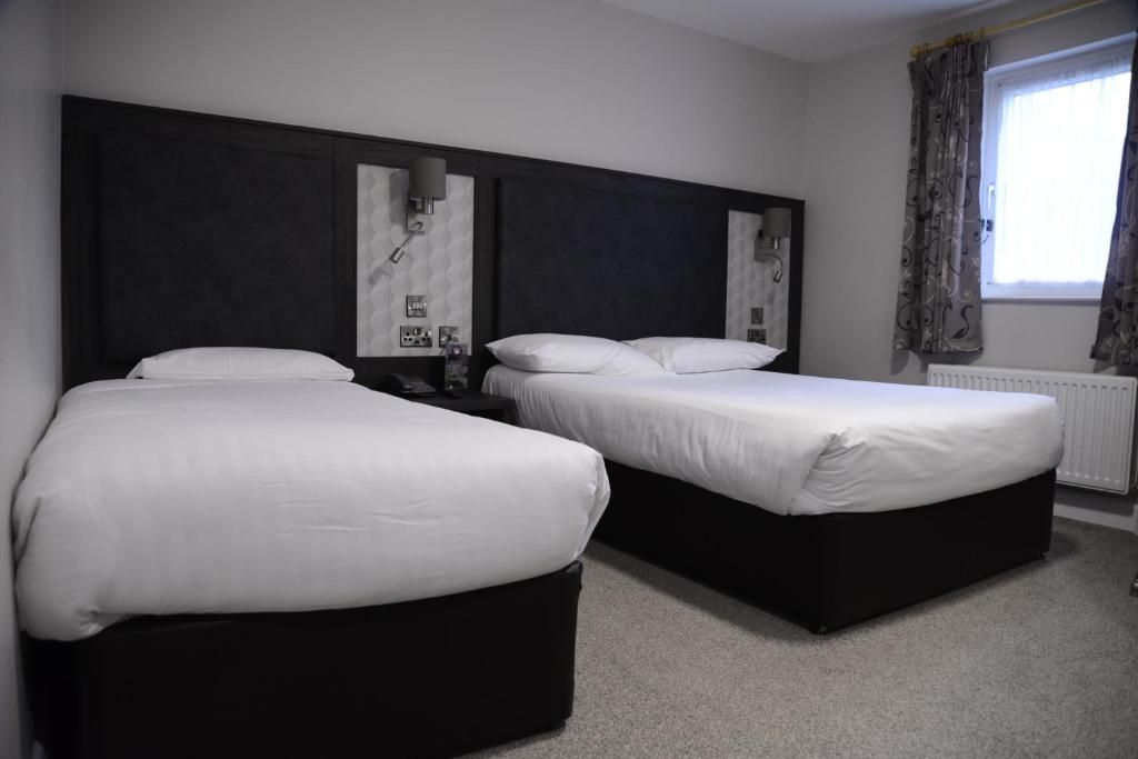 A hotel room with two beds, a large headboard, a window with curtains, and a radiator.
