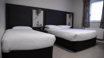A hotel room with two beds, a large headboard, a window with curtains, and a radiator.