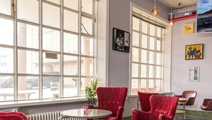 A modern interior with large windows, red upholstered chairs, a round table, and a radiator. - Hostel B47 (Reykjavik)