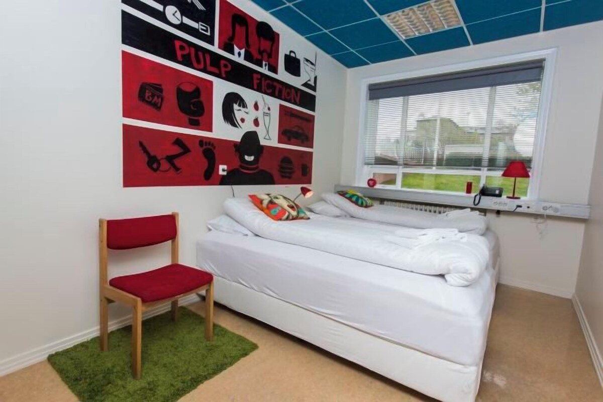 A bedroom with a bed, a chair, a window, and wall art.