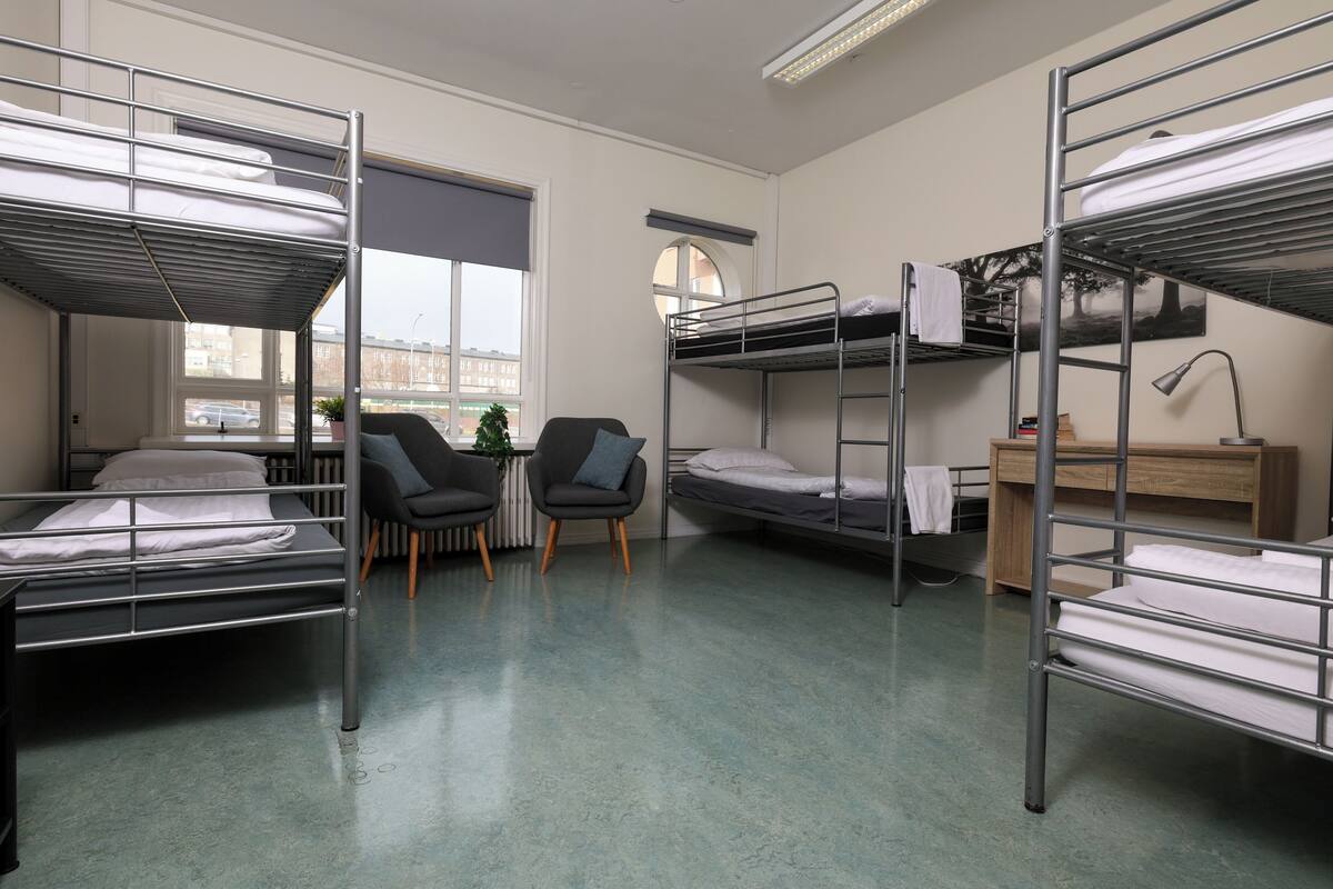 Un dormitorio con literas, un escritorio, una silla y una ventana con vistas a edificios.
